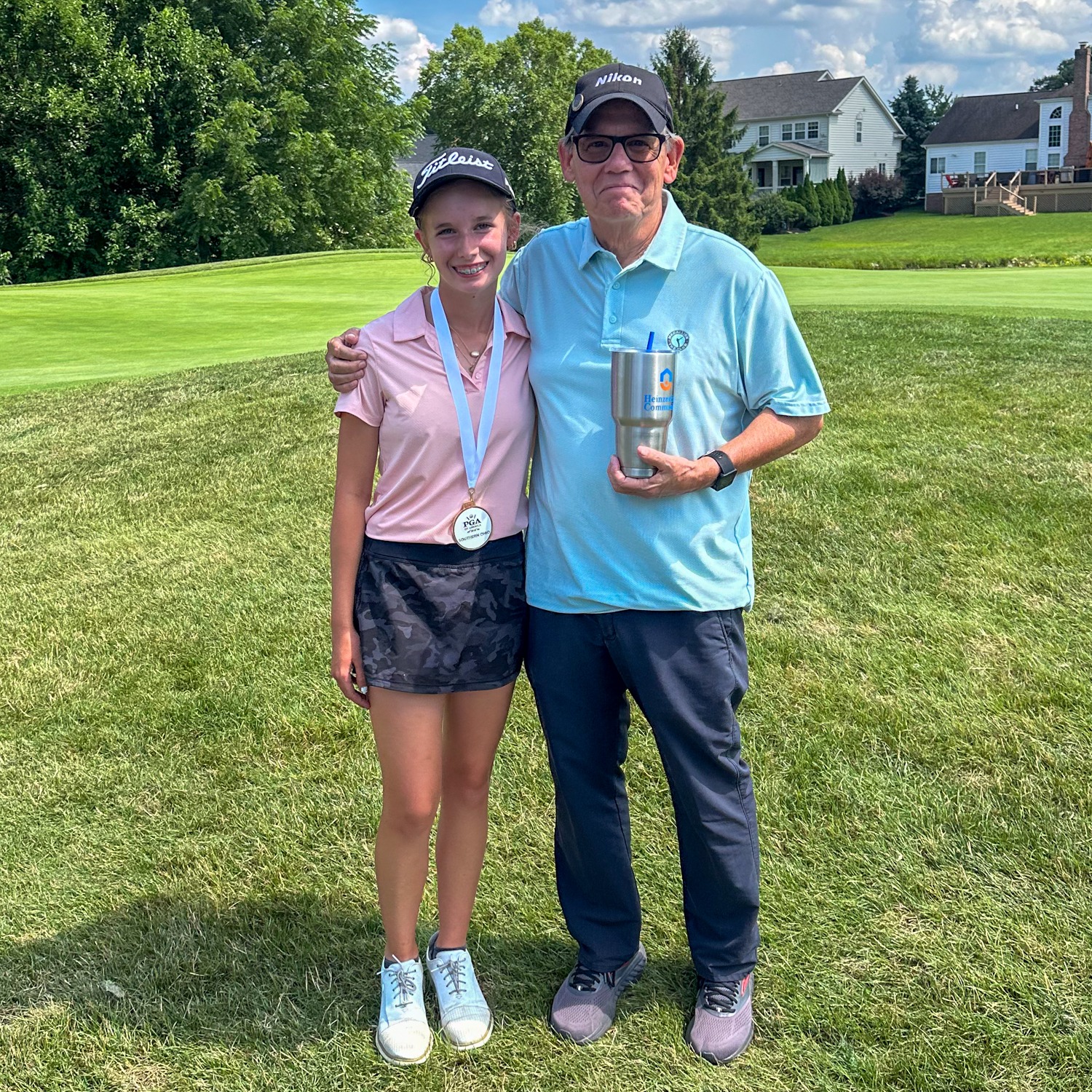 Olivia Huffman wearing a golf medal while posing with her proud grandfather on the course