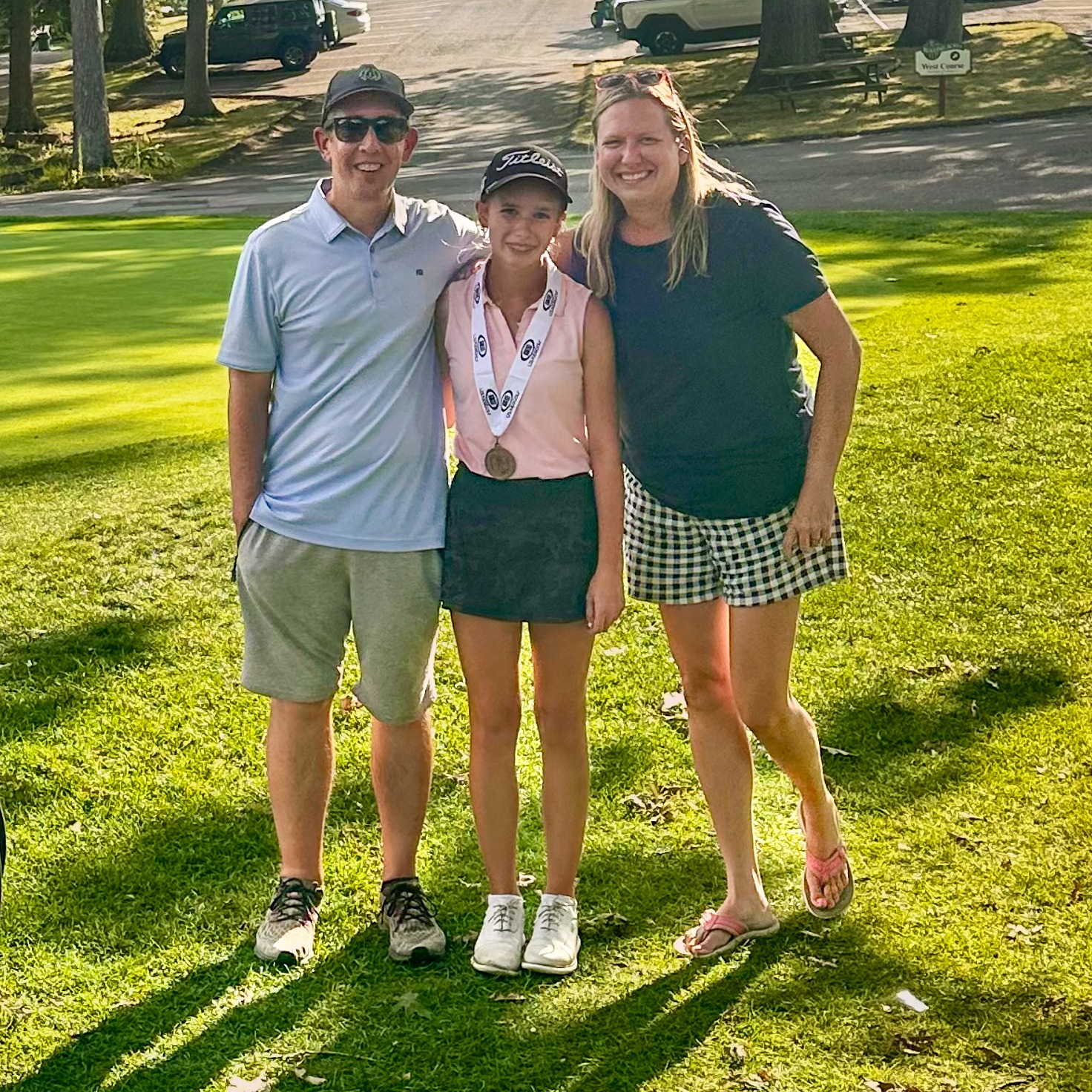 Olivia Huffman wearing a gold medal while standing with her proud parents on a golf course